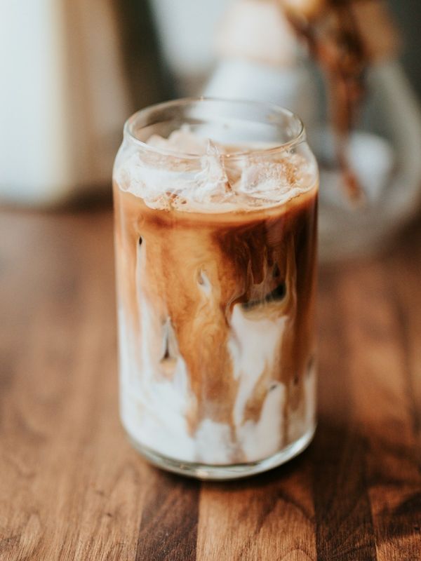 Iced latte in a clear glass with milk and espresso swirling together over ice on a wooden table.