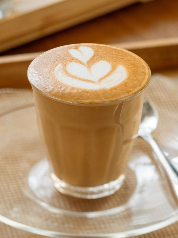 Hot latte in a white cup with heart-shaped latte art, served on a saucer on a wooden table.