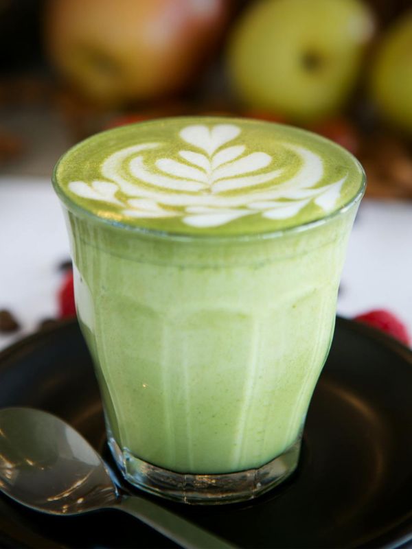 Hot matcha latte in a glass with white latte art, served on a black saucer with a spoon.