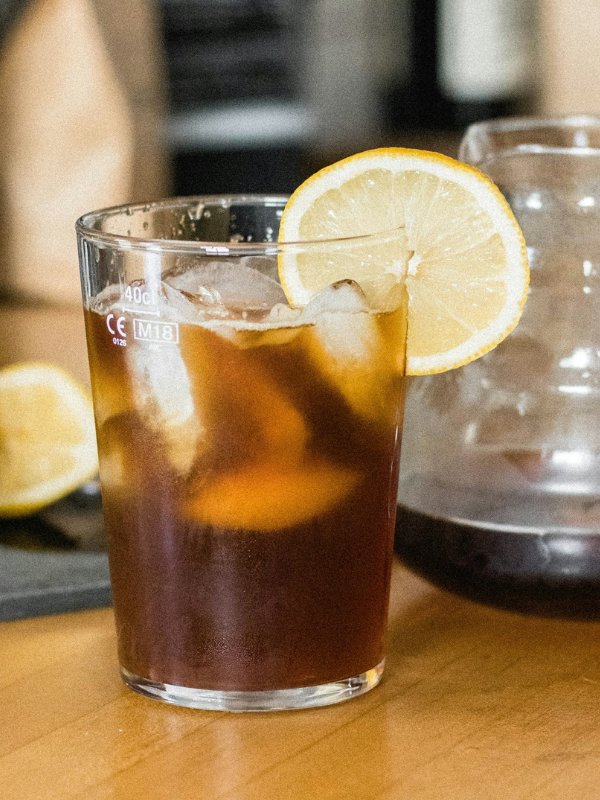 Iced black coffee with a lemon slice garnish in a clear glass.