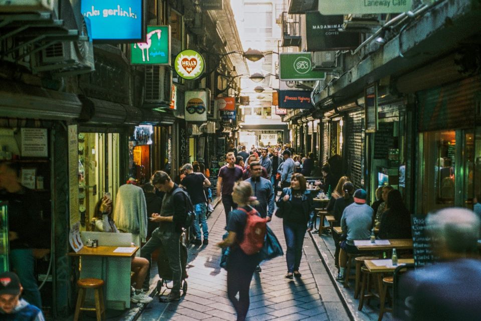 A view of a narrow laneway in Melbourne filled with outdoor tables and patrons, representing the city’s independent espresso culture.